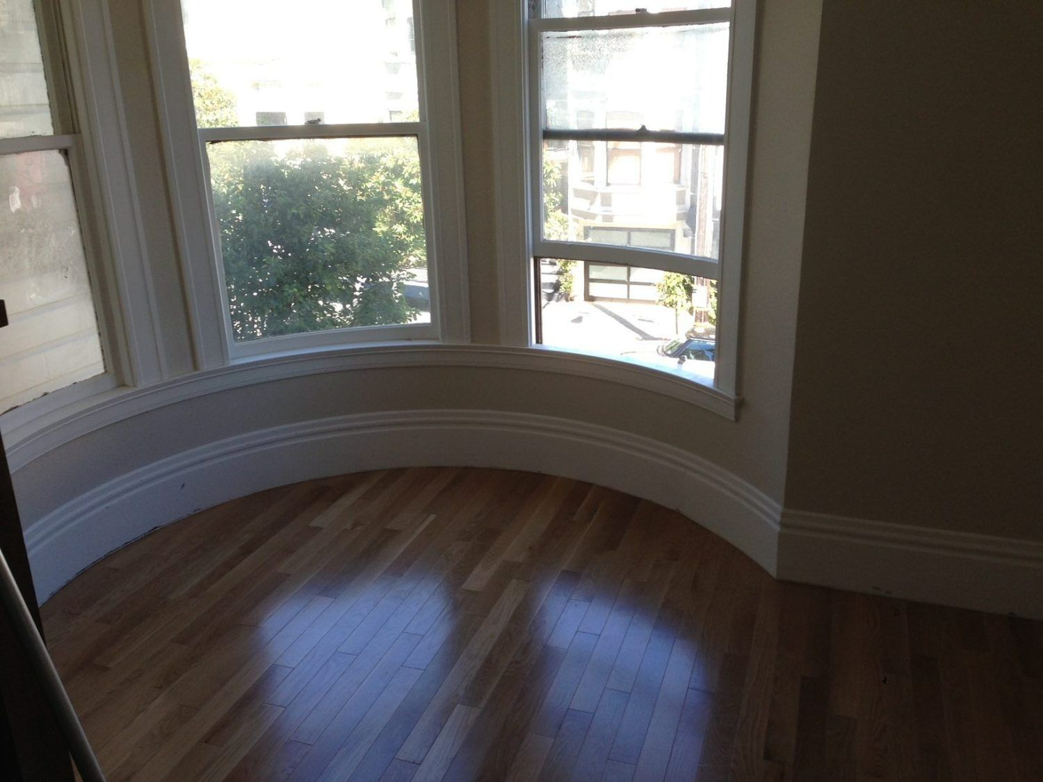 Bay window with hardwood floors. Sunlight streams through the windows, illuminating the curved baseboard.