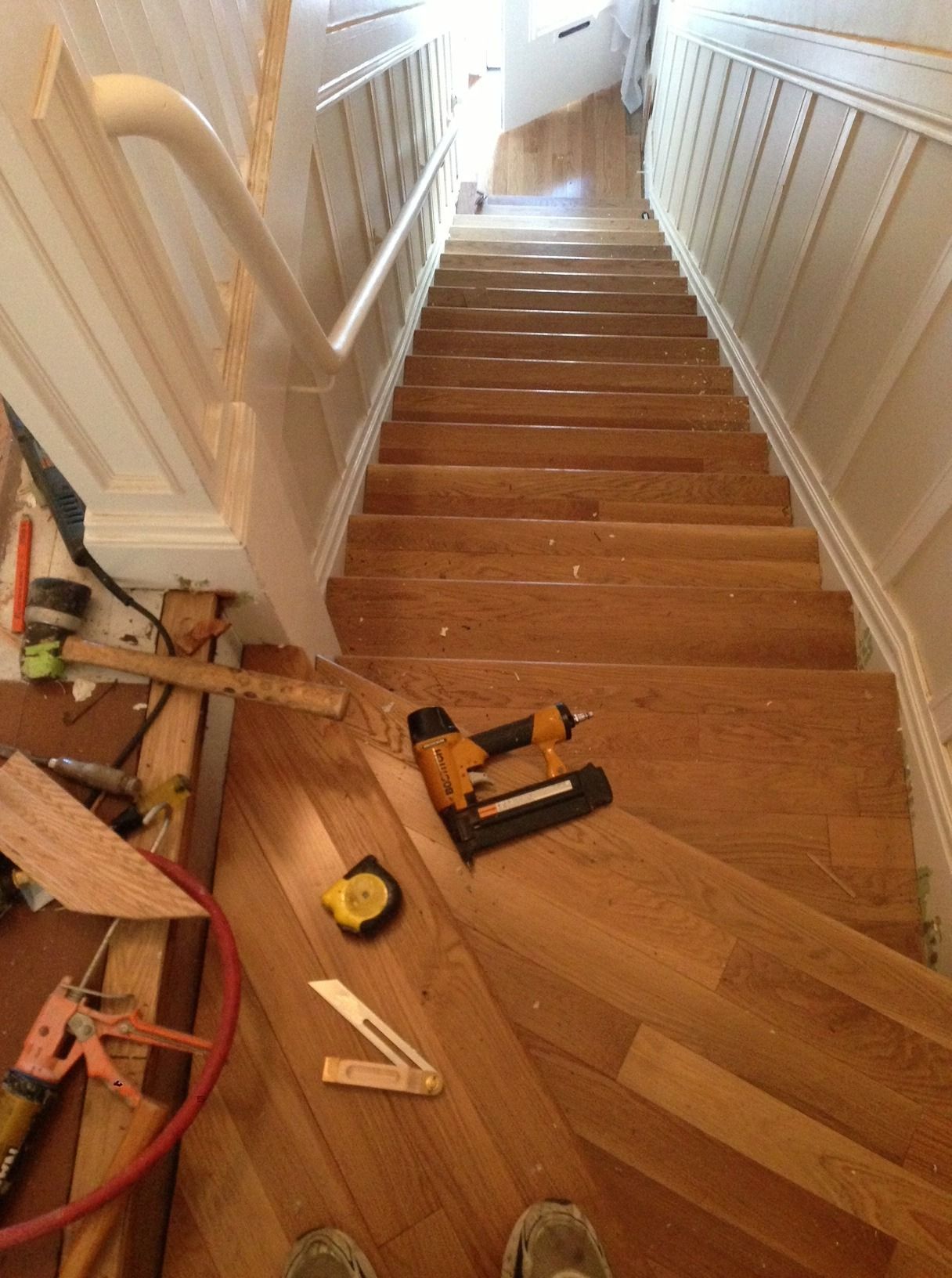 Wooden staircase being renovated, with tools on the landing and new flooring partially installed.