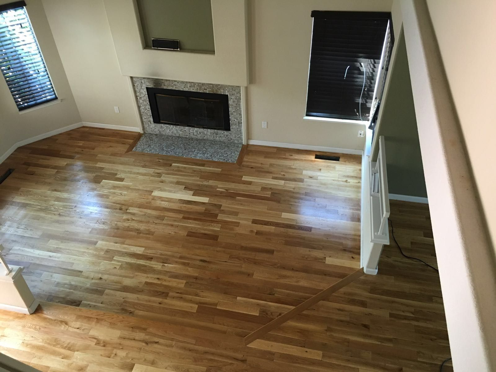 Hardwood floors in a living room with a fireplace, blinds, and a staircase visible.