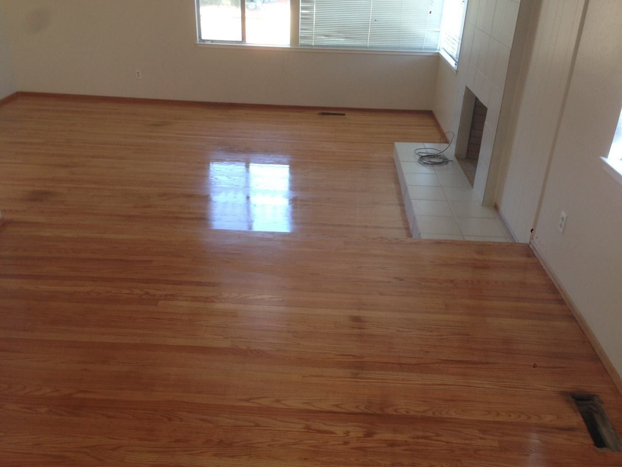 Wooden floor in a room with a fireplace and a window, reflecting light.