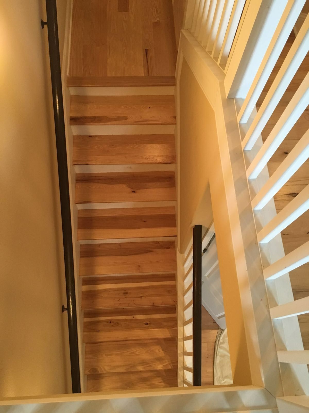 Wooden staircase with white banister on one side, dark handrail on the wall.