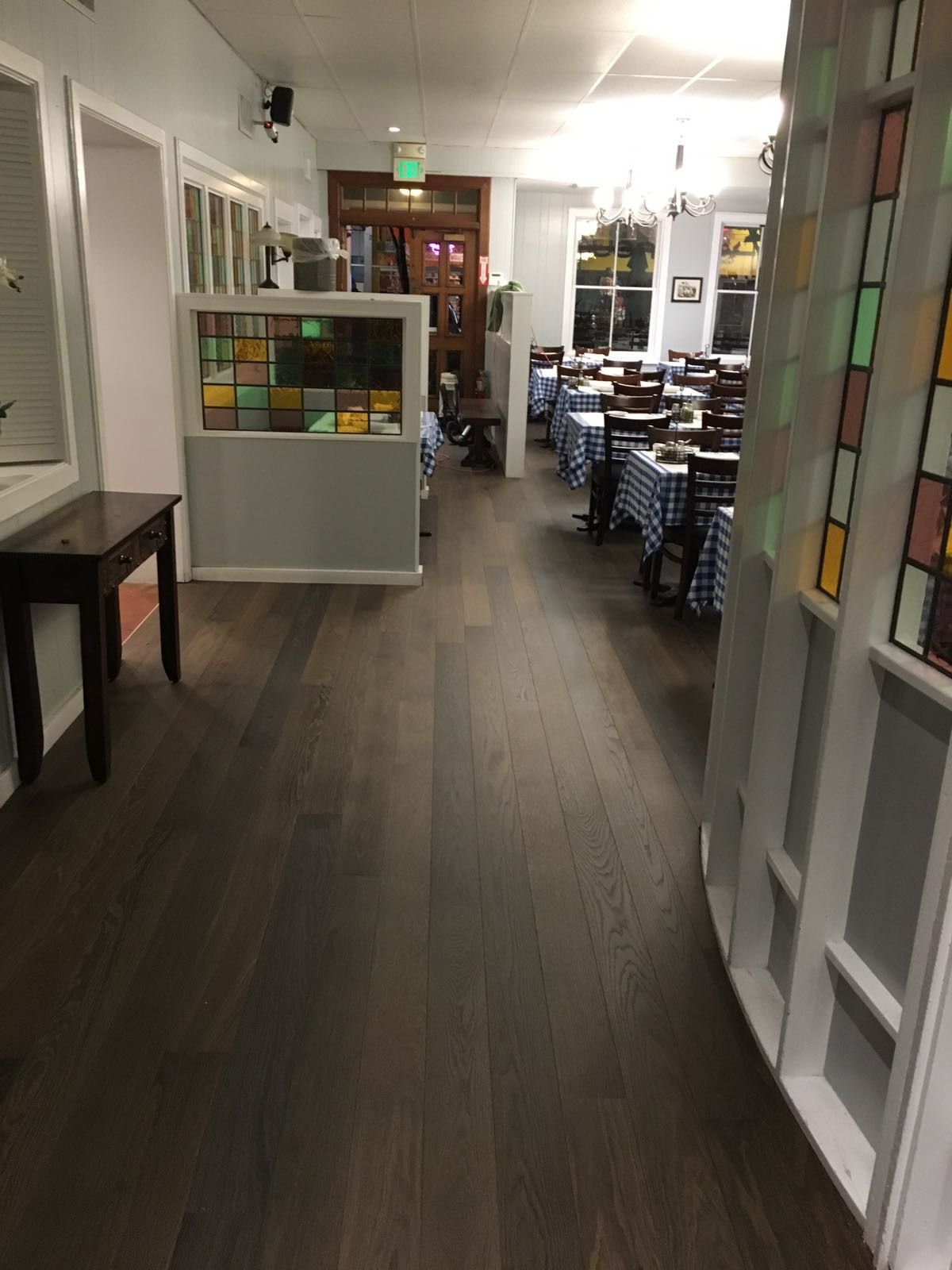 Interior view of a restaurant. Dark wood floor, tables with blue checkered tablecloths. Stained glass window accents.