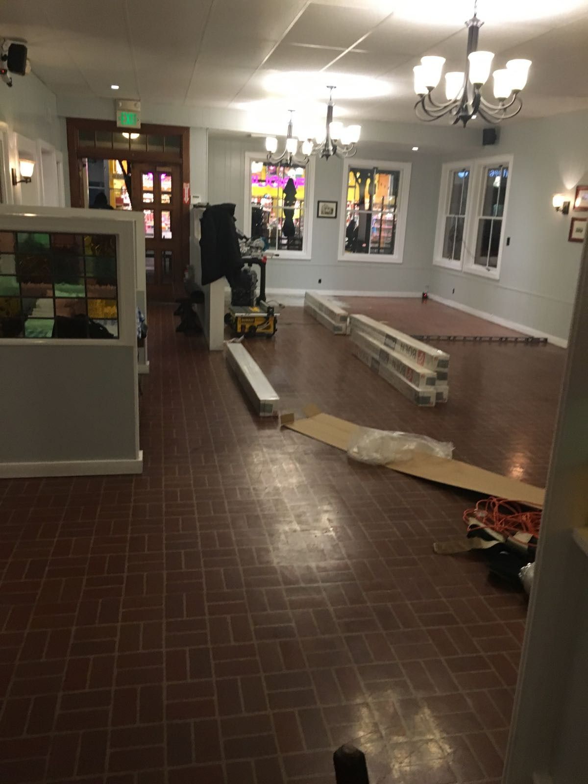 Empty room with brick floor, chandeliers, and stained glass windows. Construction materials scattered about.