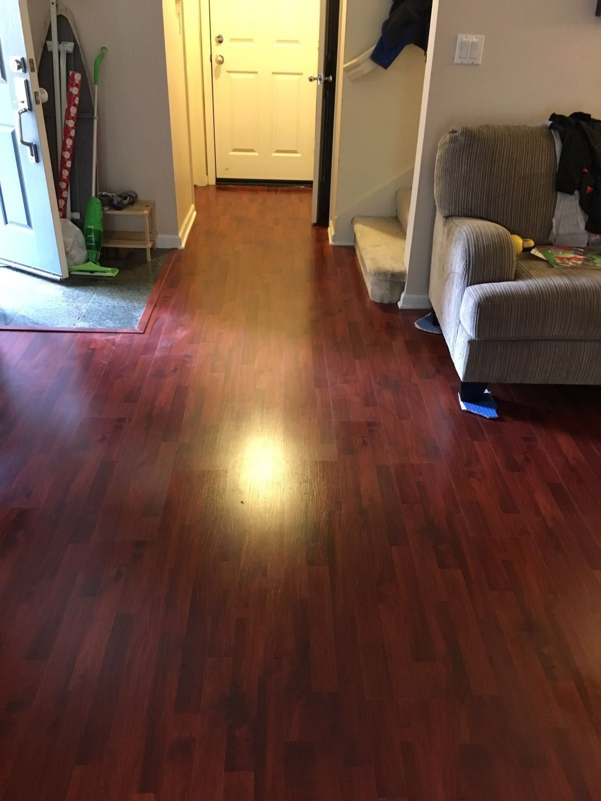 Reddish-brown hardwood floor hallway leading to a white door. A beige couch is on the right.