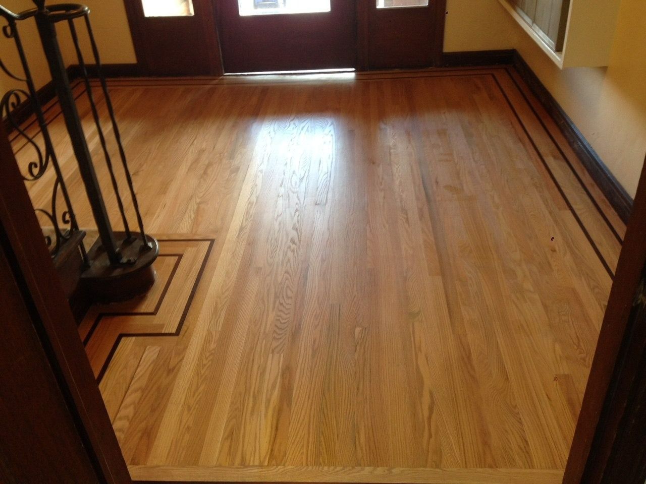 Wooden floor with a dark border, leading toward a dark entryway with a staircase and a window.