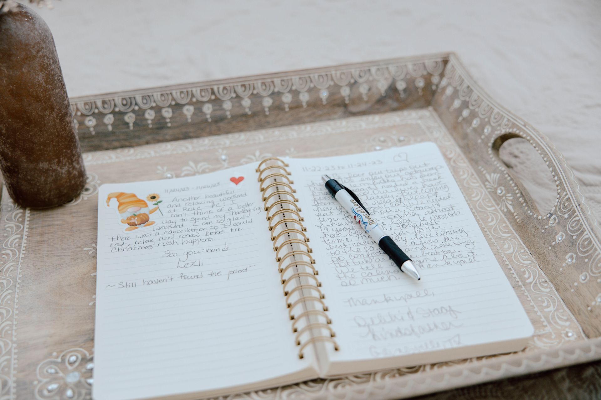 Open notebook on a decorative tray with a black pen resting across the pages.