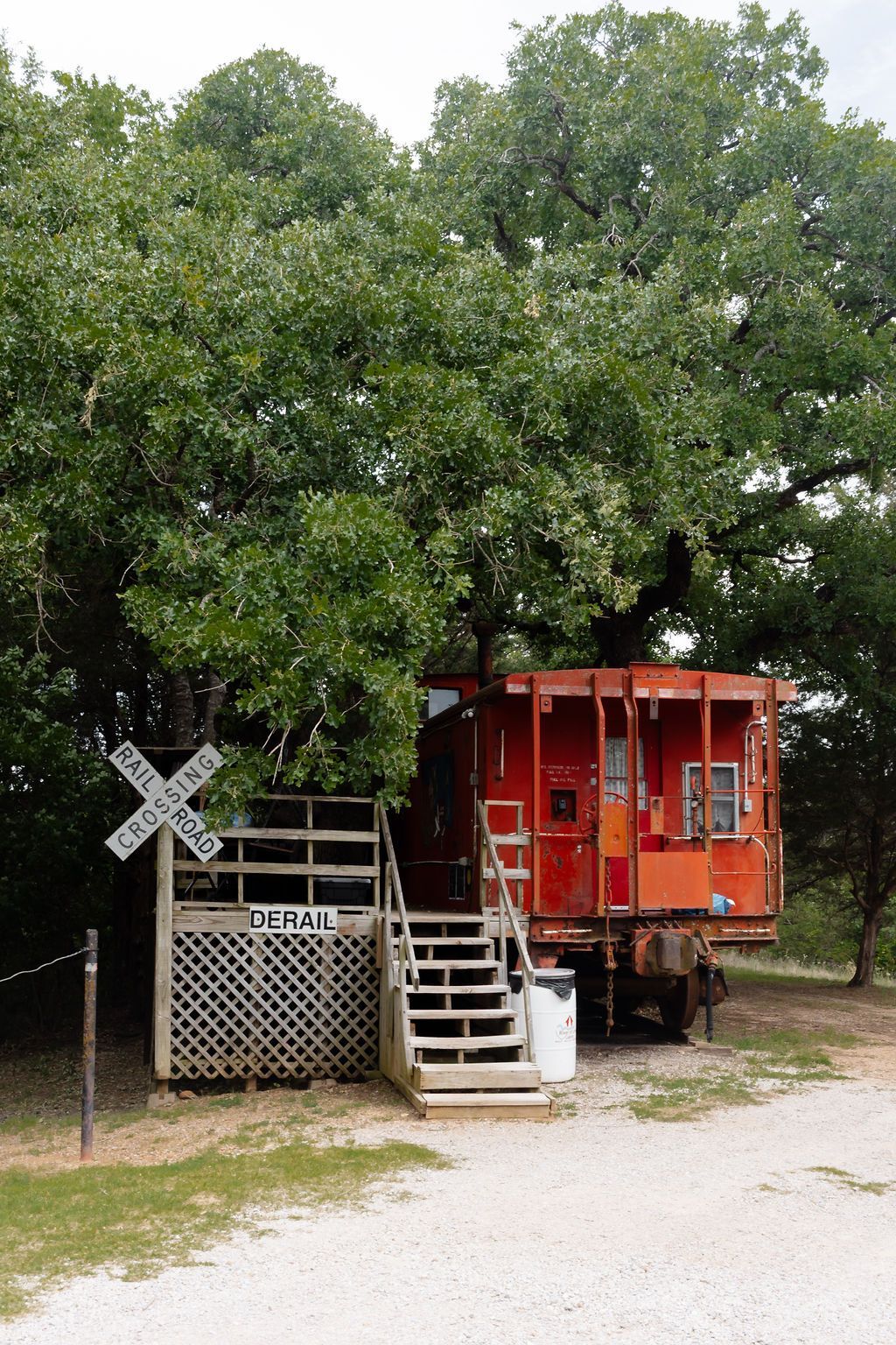 Red caboose-style train car with stairs beside a railroad crossing under trees