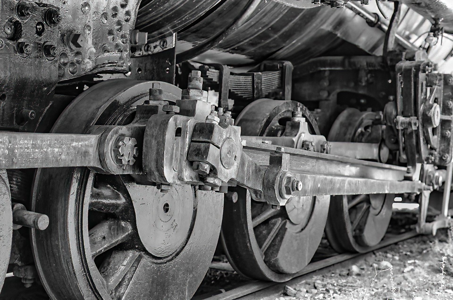 Black-and-white close-up of a steam locomotive’s wheels and connecting rods in a maintenance shed