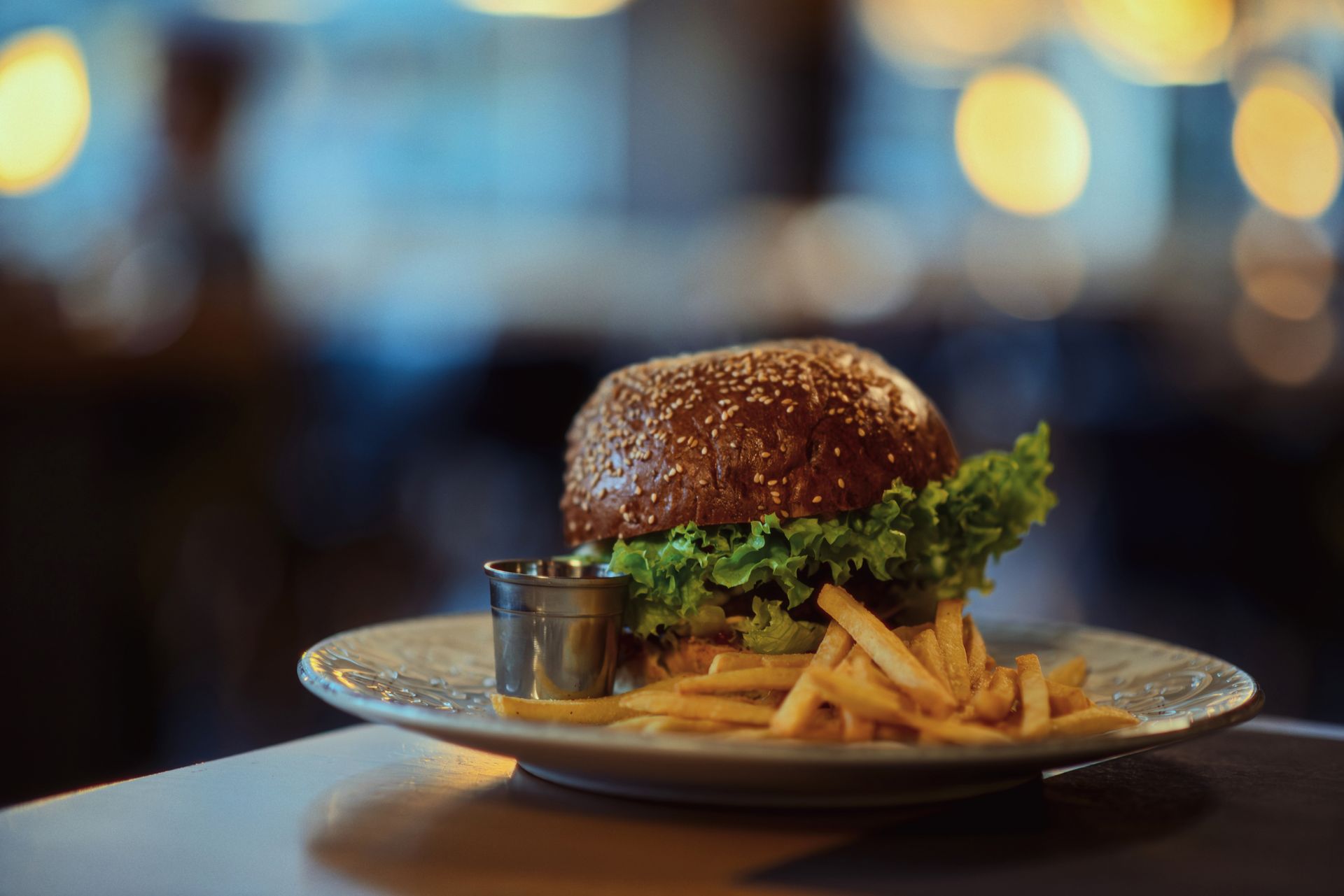 Burger and fries on a plate with a small dipping cup, set against a softly blurred restaurant background