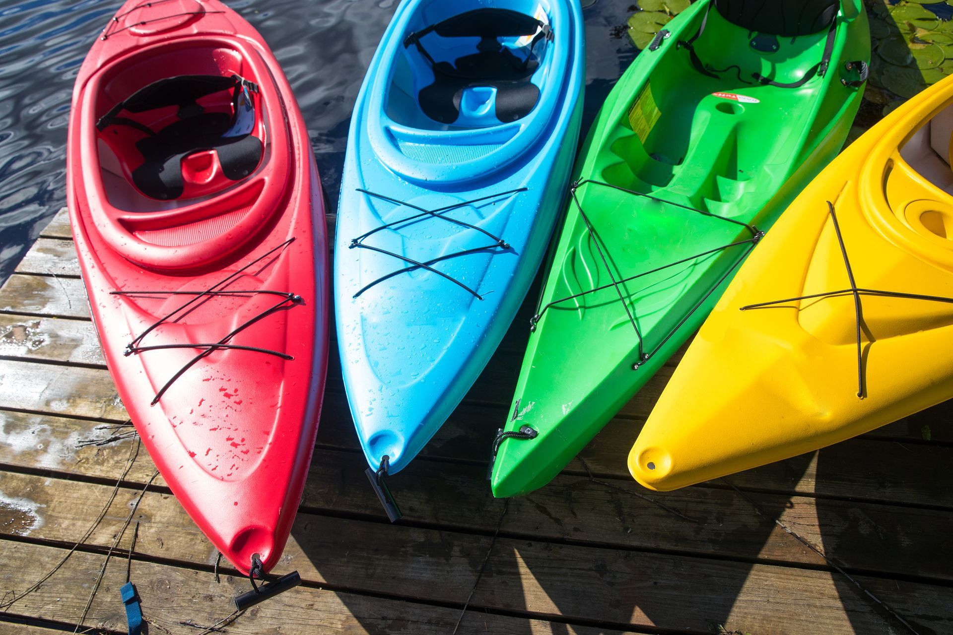 Colorful kayaks—red, blue, green, and yellow—lined up on a wooden dock.