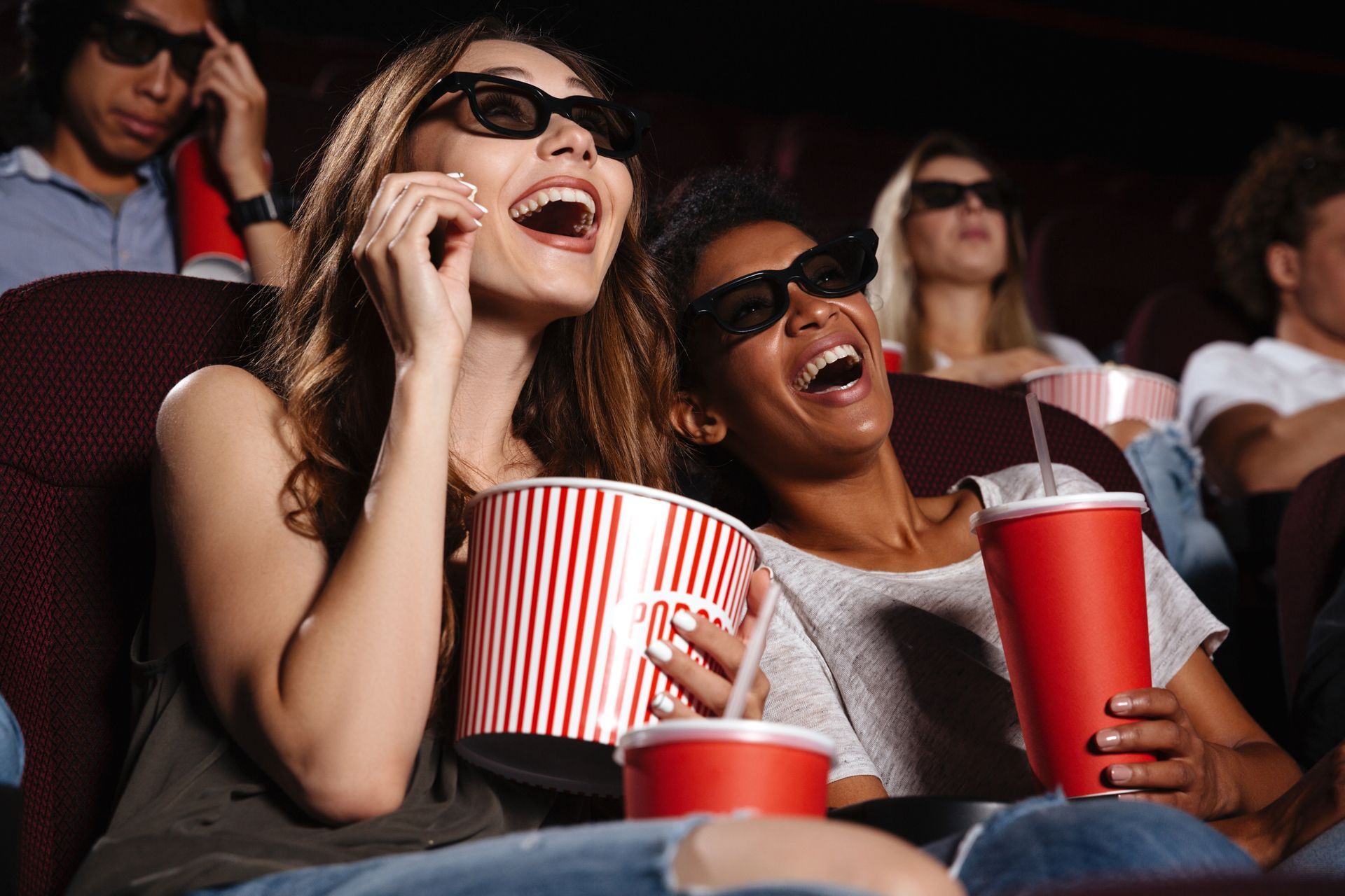 Friends laughing with popcorn and drinks at a movie theater