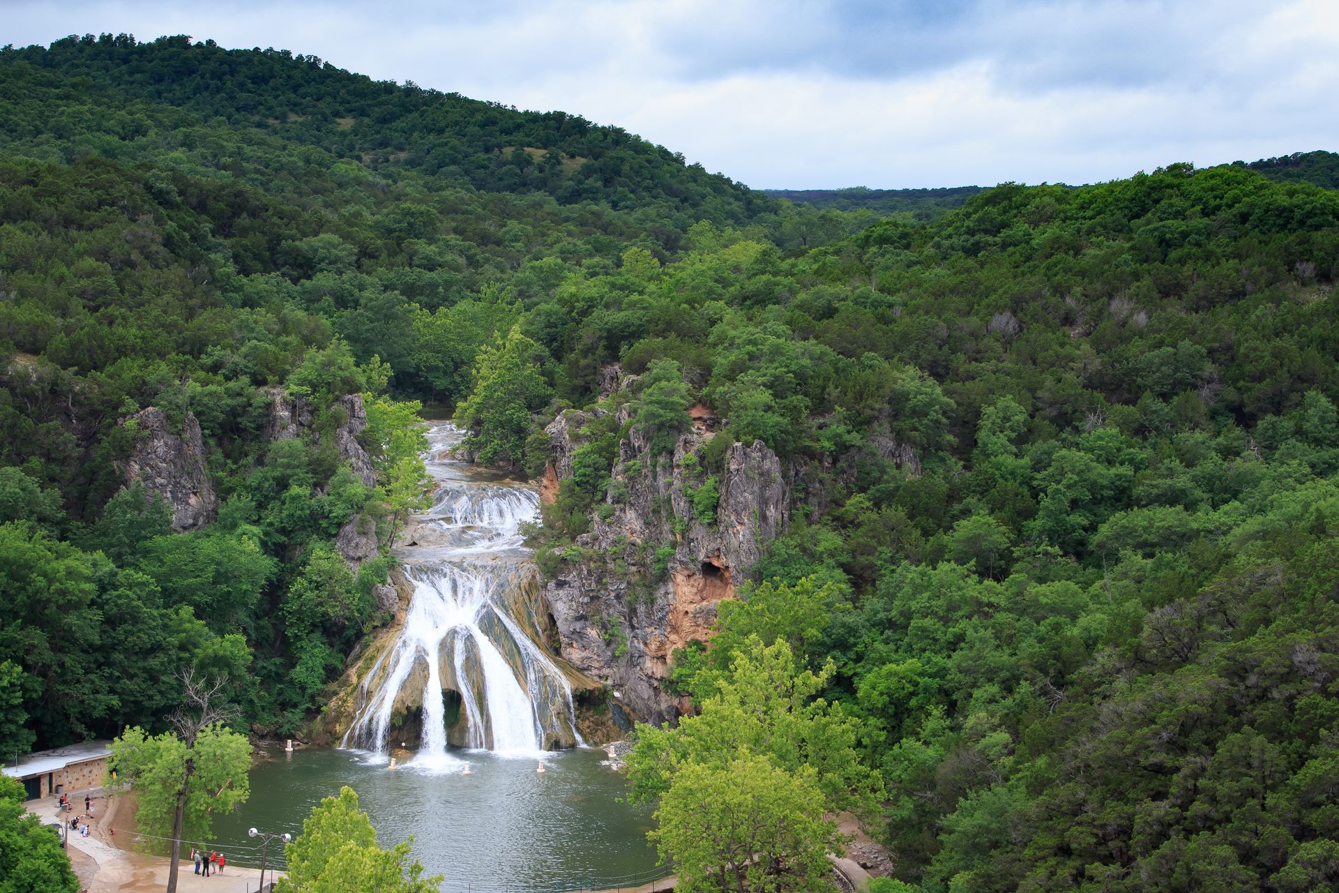 Waterfall cascading into a pool amid dense green forest and rocky cliffs