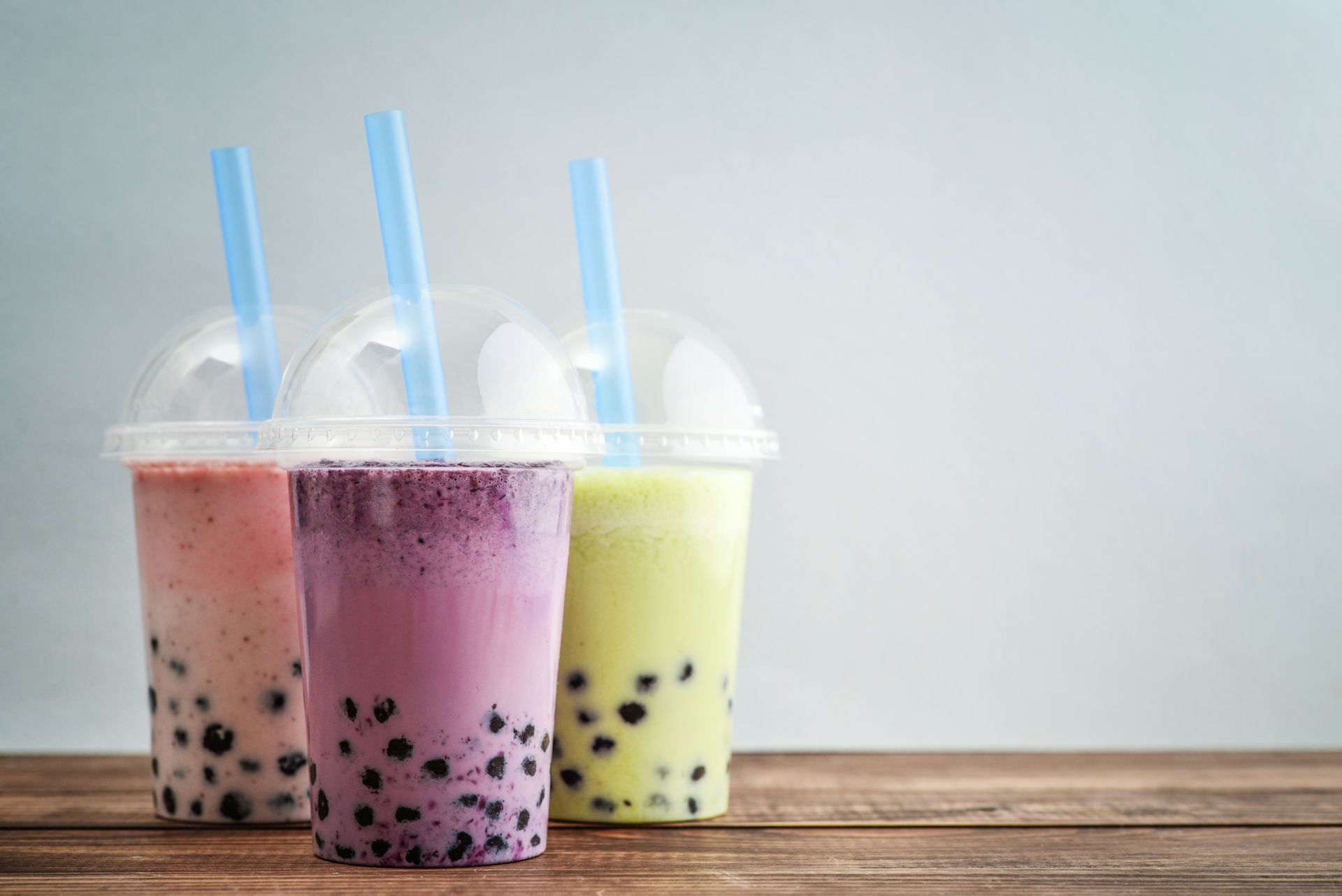 Three colorful bubble tea drinks with straws on a wooden table