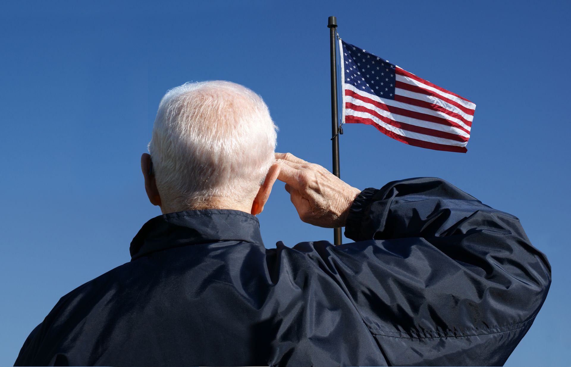 Man saluting the U.S. flag against a clear blue sky