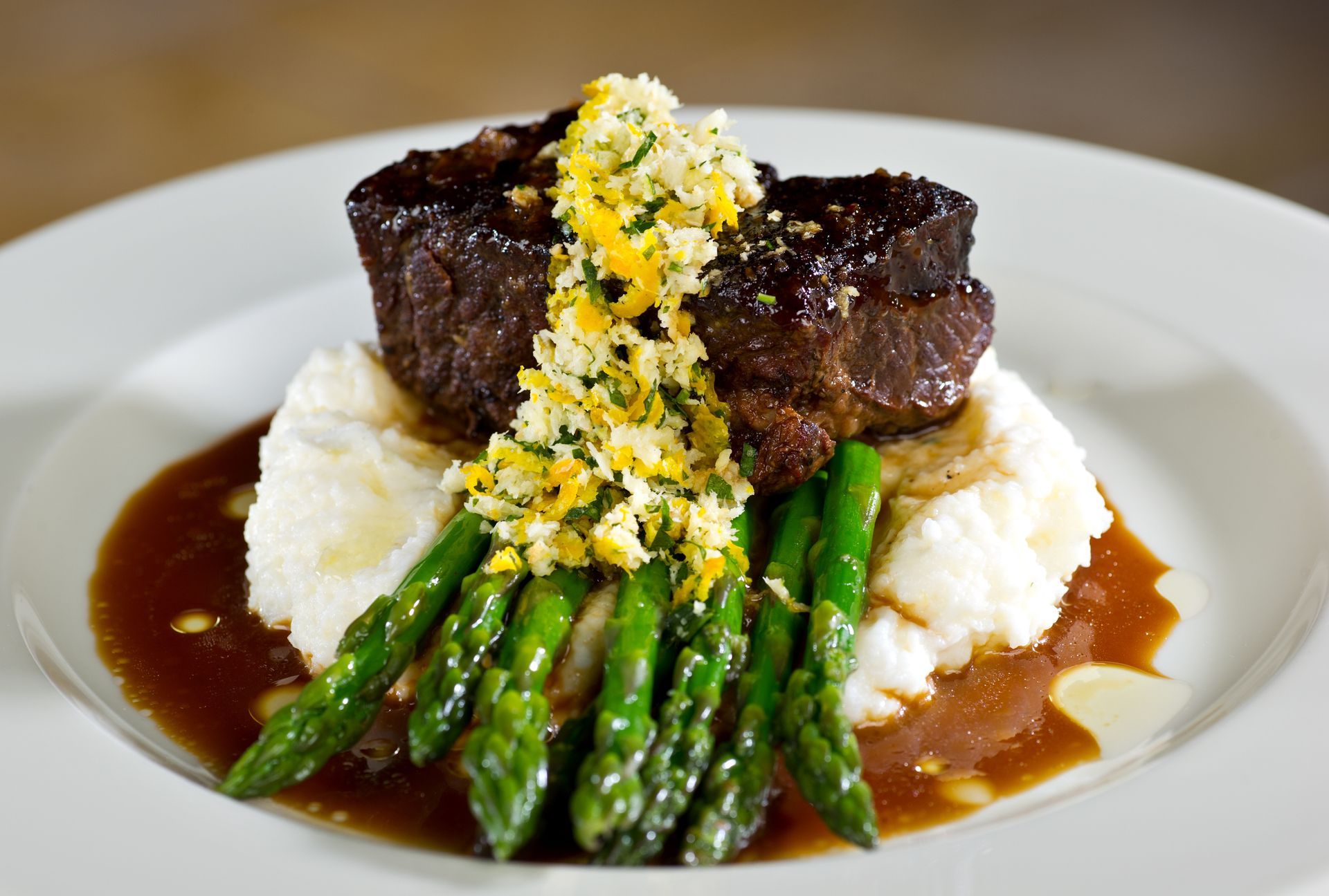 Seared steak over mashed potatoes with asparagus and brown sauce, topped with lemon zest