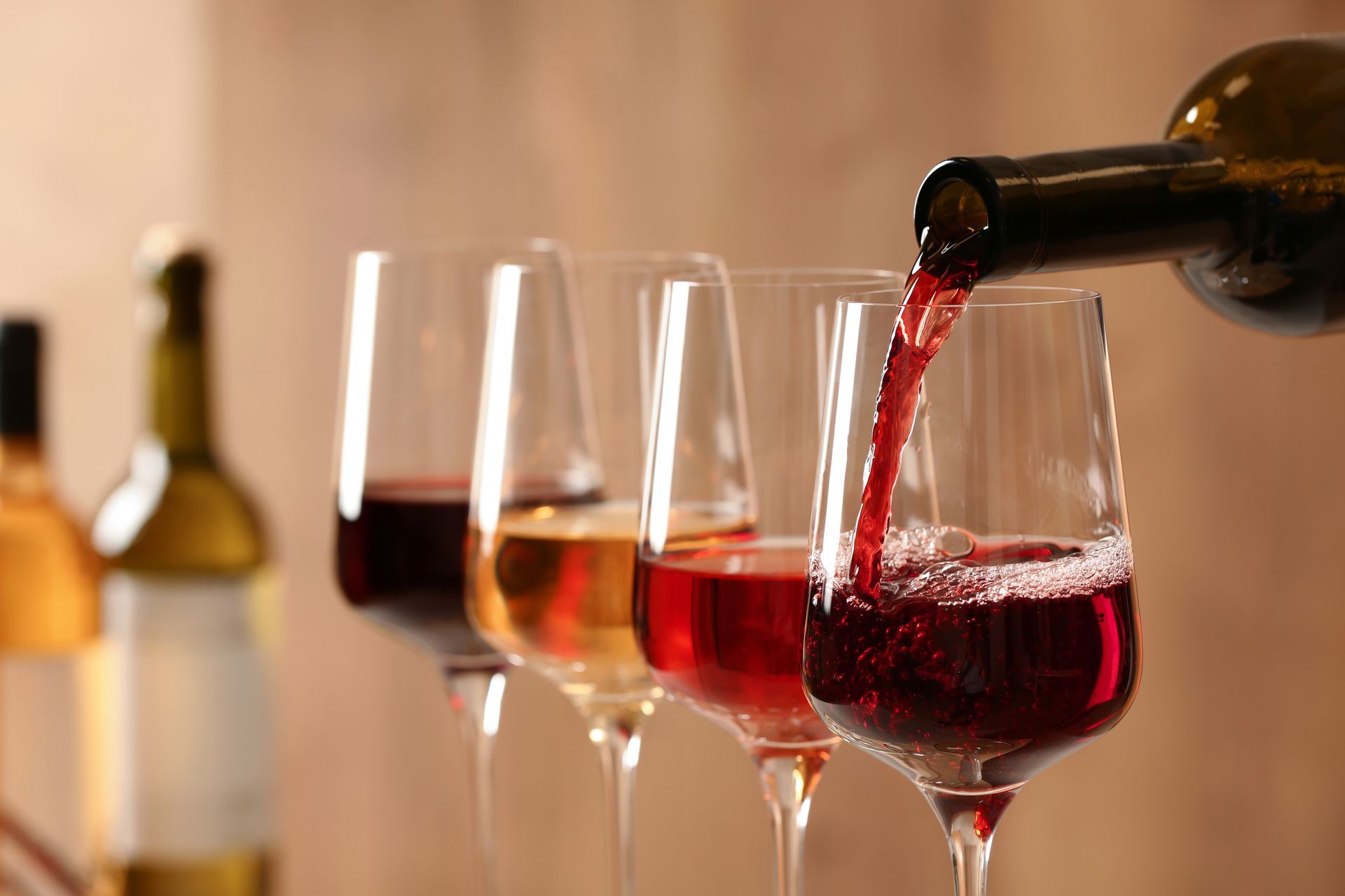 Wine being poured into a glass among several red wine glasses on a table