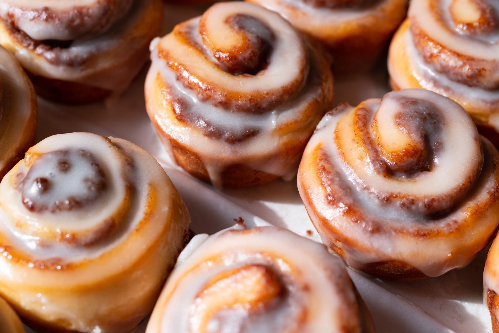 Iced cinnamon rolls with white glaze, arranged closely on a tray