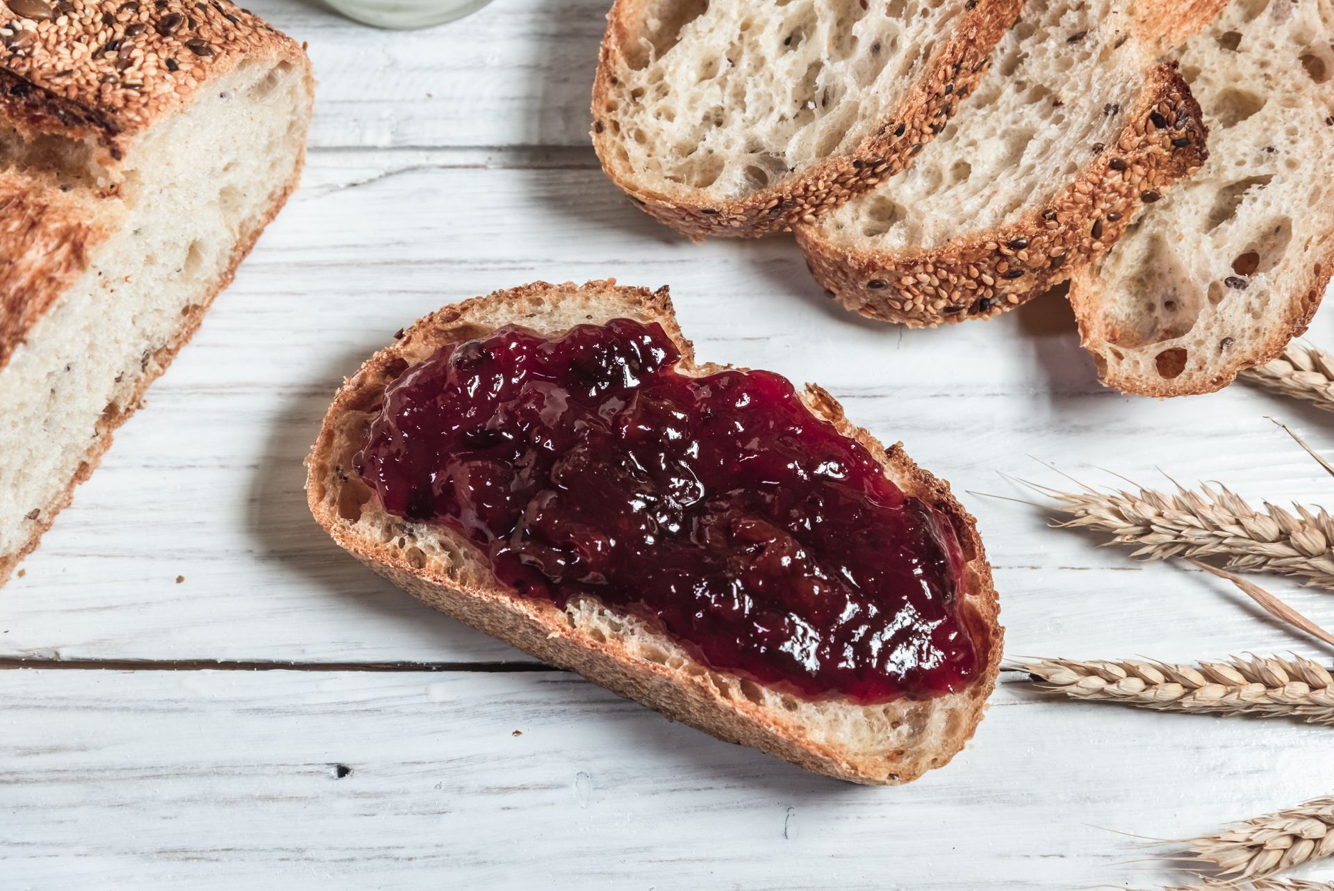 Rustic bread slices with dark berry jam on a white wooden surface