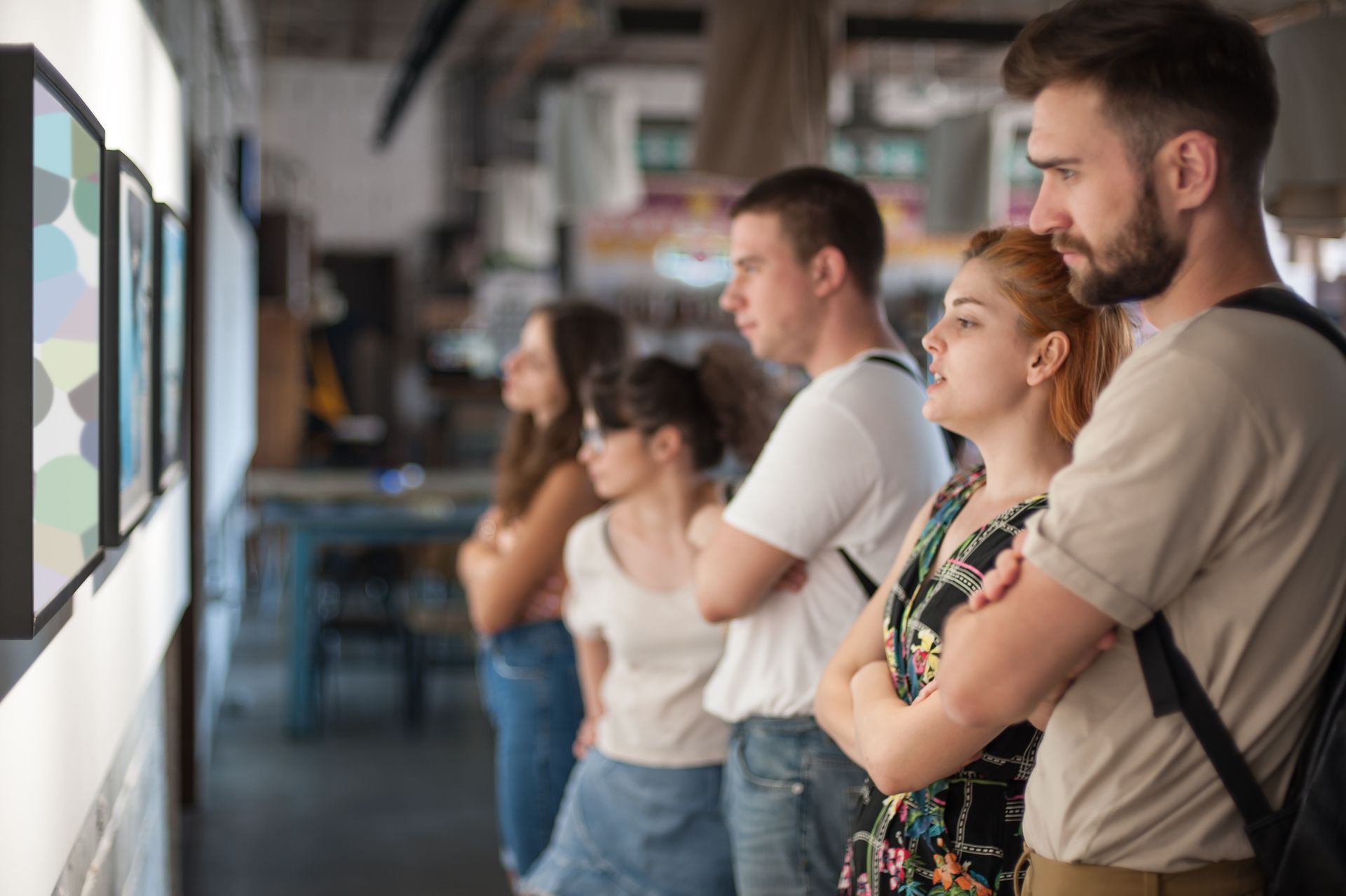 People viewing framed art in a gallery, standing in a row with arms crossed