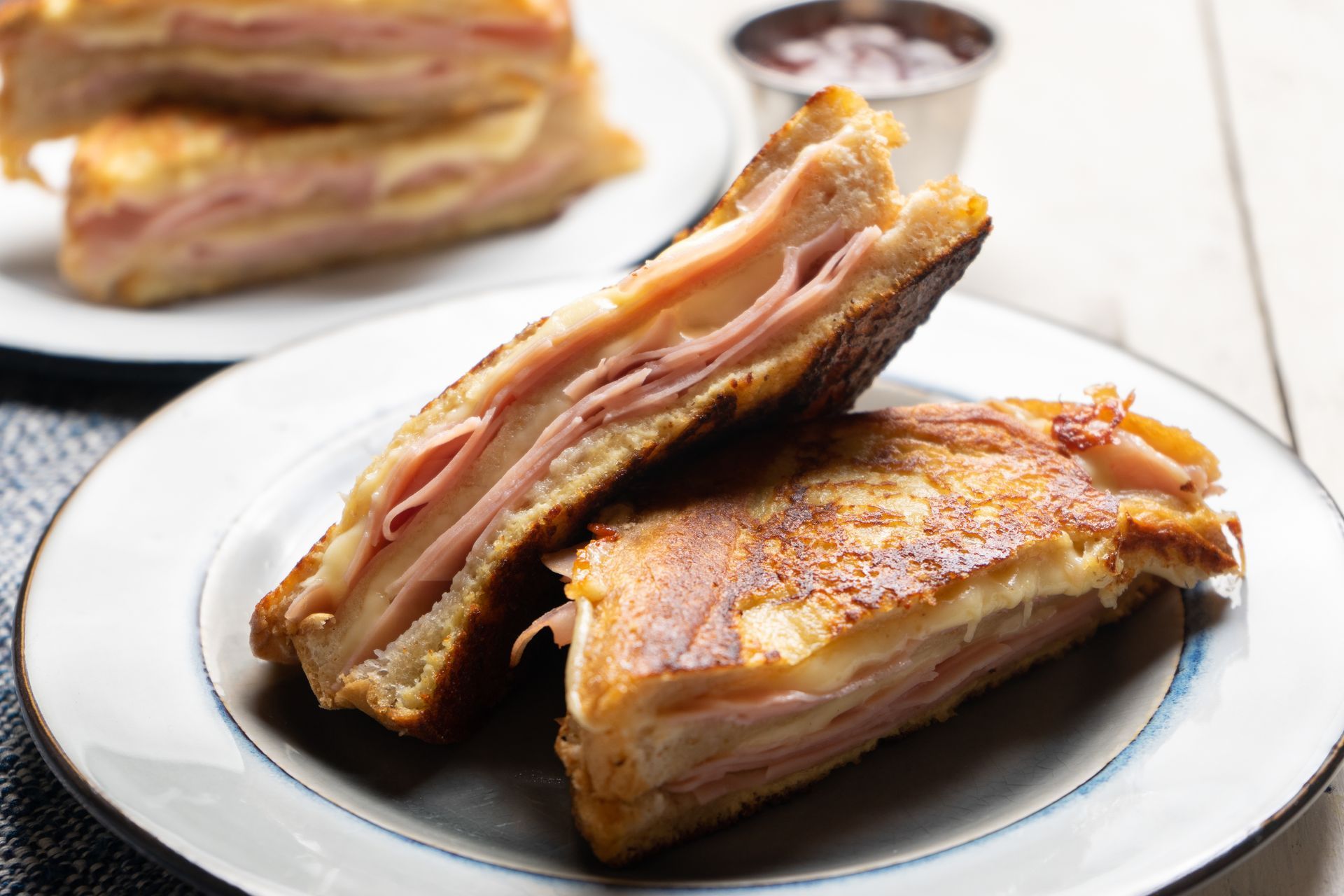 Grilled ham and cheese sandwich halves on a white plate with a dipping sauce