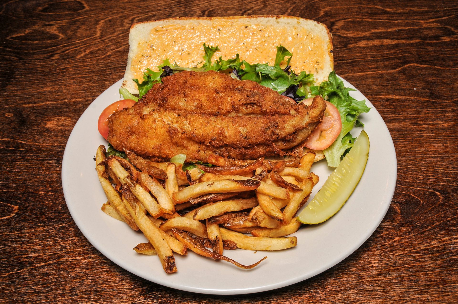 Fried fish sandwich with fries, lettuce, and a pickle on a white plate