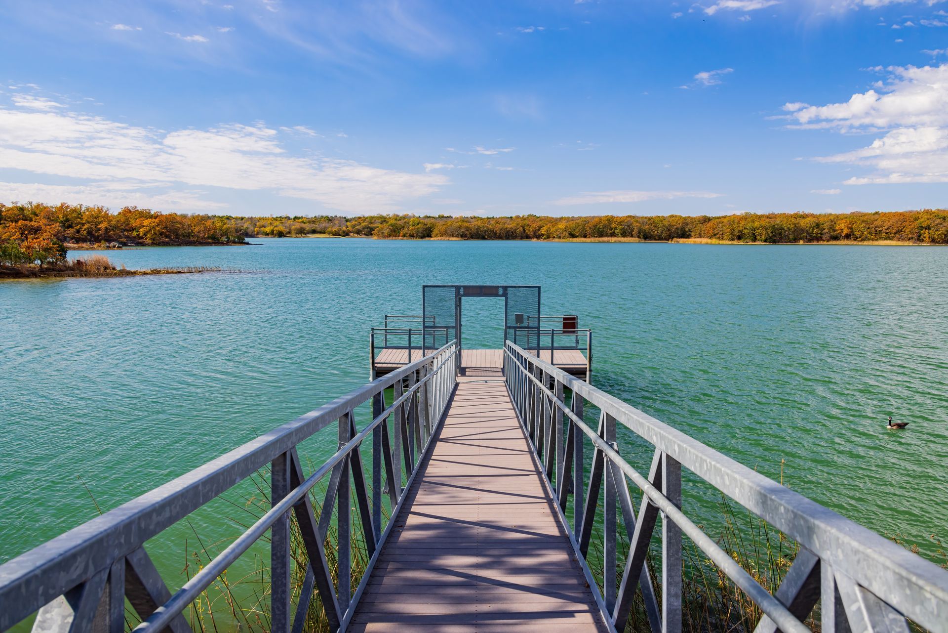Wooden pier extending into a calm blue lake under a partly cloudy sky