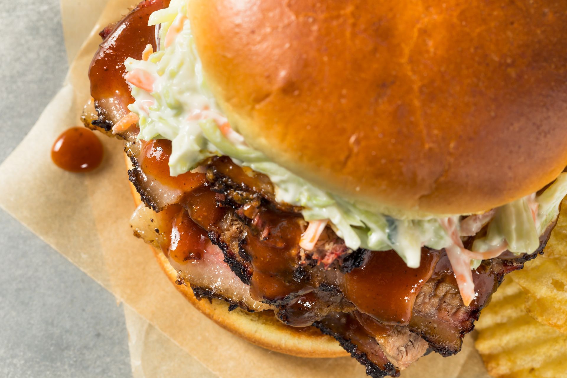 Close-up of a barbecue burger with shredded lettuce on a bun, served on parchment paper.