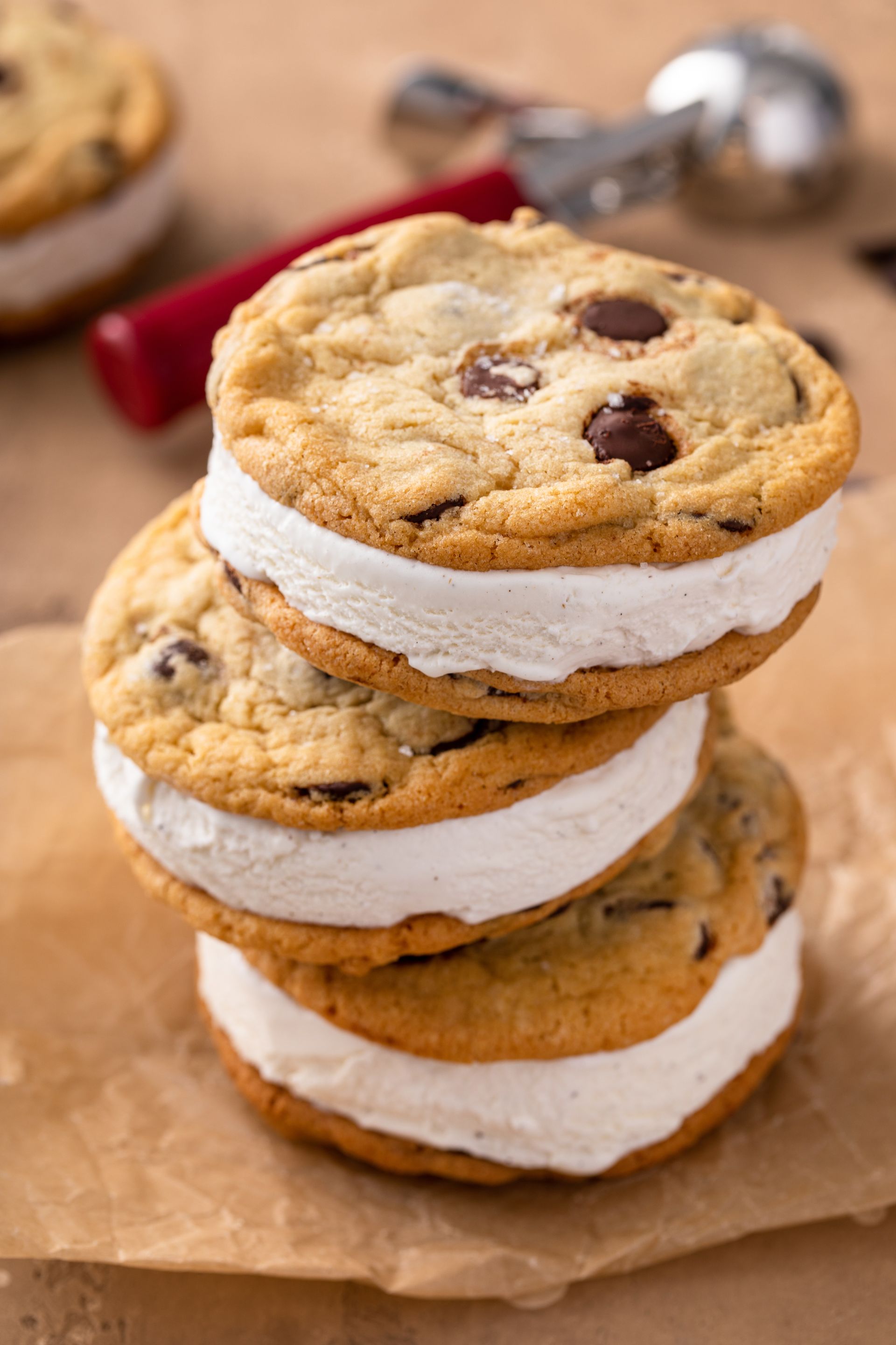 Stack of chocolate chip ice cream sandwiches on parchment paper, with a blurred red berry in the background