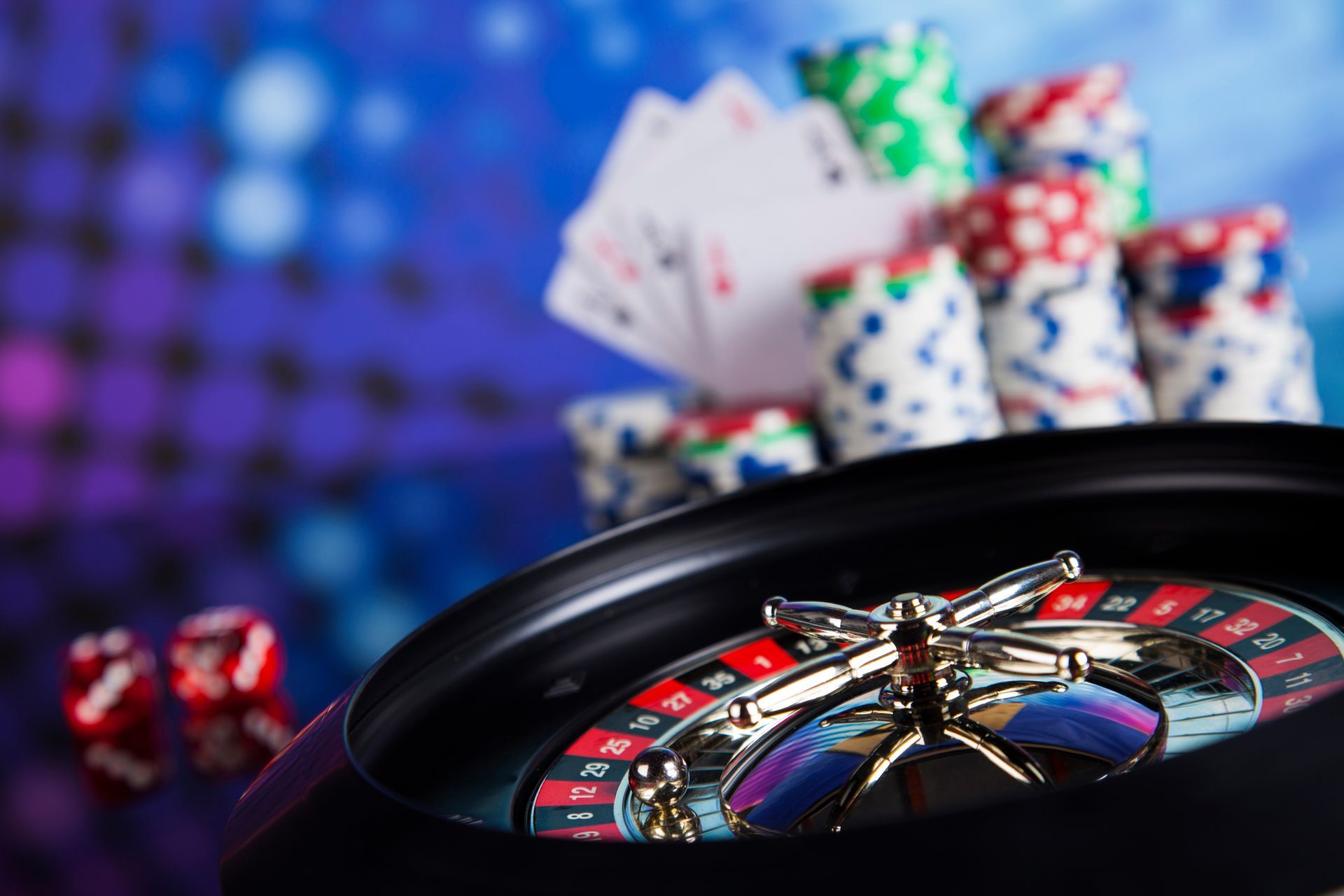 Roulette wheel with playing cards and poker chips on a casino table, purple lights in the background