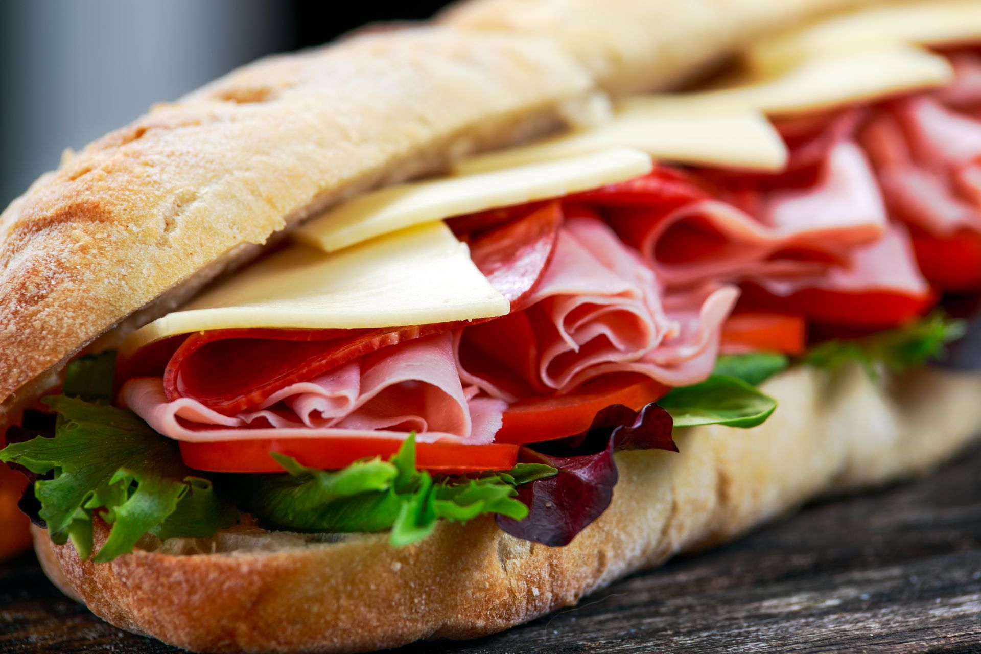 Toasted sandwich with sliced ham, cheese, and lettuce on a wooden surface