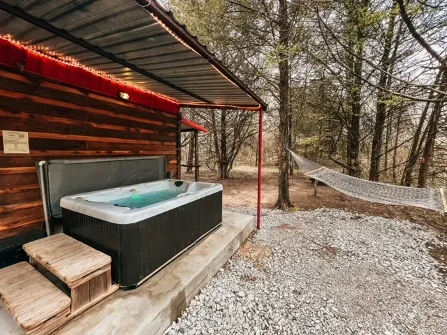 Hot tub on a cabin deck beside a hammock in a wooded outdoor setting