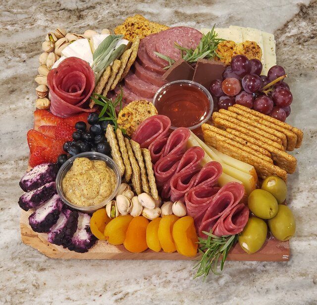 Charcuterie board with meats, cheeses, crackers, grapes, olives, nuts, and fruit on a marble surface