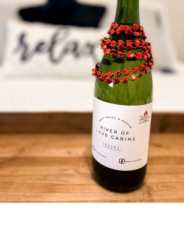 Green bottle with red beaded decoration on a wooden table, label visible in soft focus room.