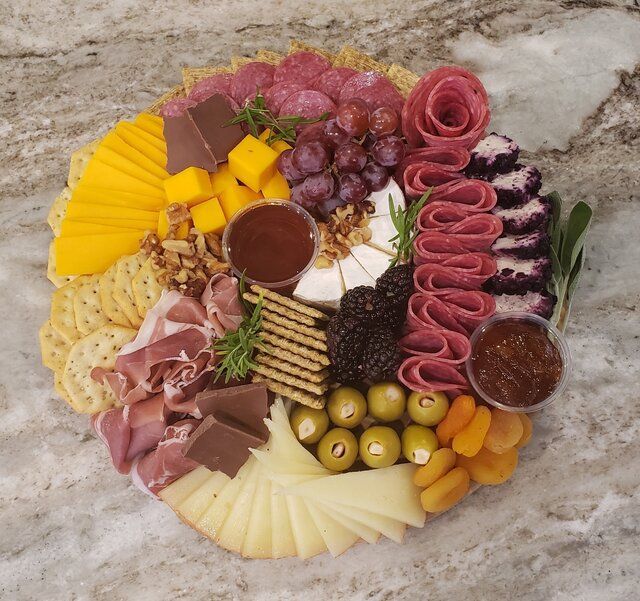 Charcuterie board with assorted cheeses, meats, olives, grapes, fruit, and crackers arranged on a stone platter