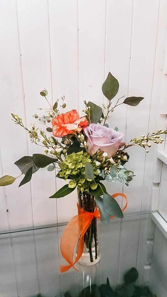 Bouquet of orange, pink, and white flowers tied with orange ribbon in a vase against a white wall
