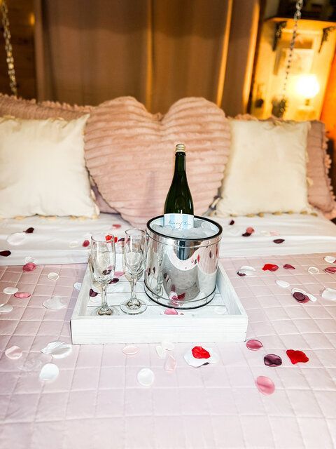 Romantic bed tray with champagne, glasses, rose petals, and heart pillows on a pink bedspread