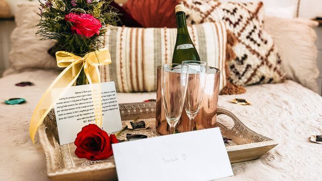 Wedding table centerpiece with roses, champagne bottle and flutes, tray, and a blank place card on a couch