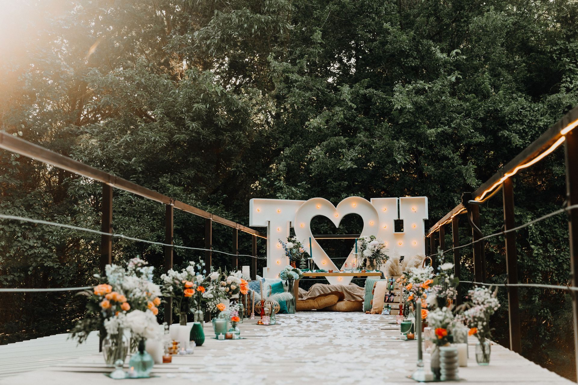 Outdoor wedding aisle with white flowers, candles, and a heart-shaped floral backdrop under trees