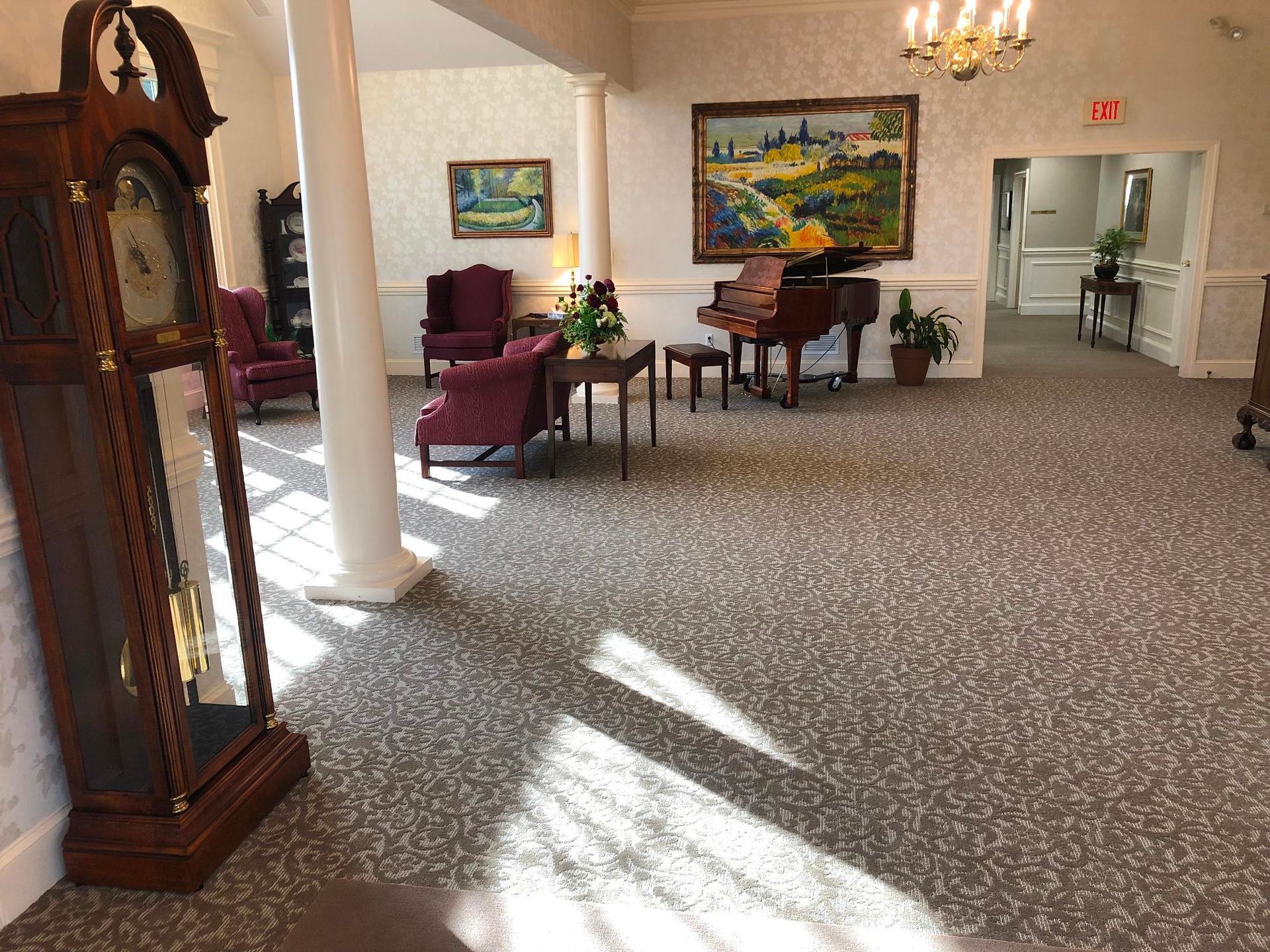Lobby seating area with chairs, a piano, wall art, and sunlight on patterned carpet