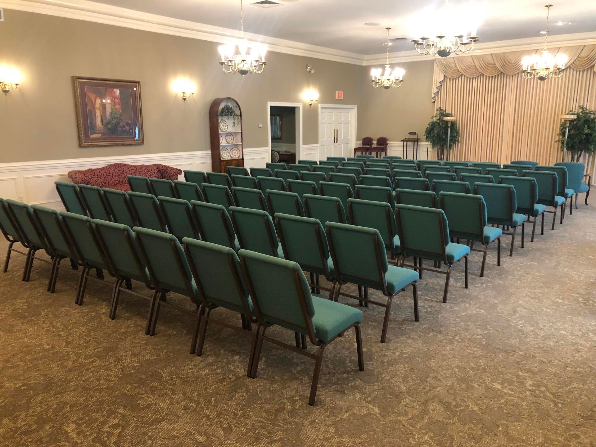 Empty meeting room with rows of green chairs facing forward on a carpeted floor.