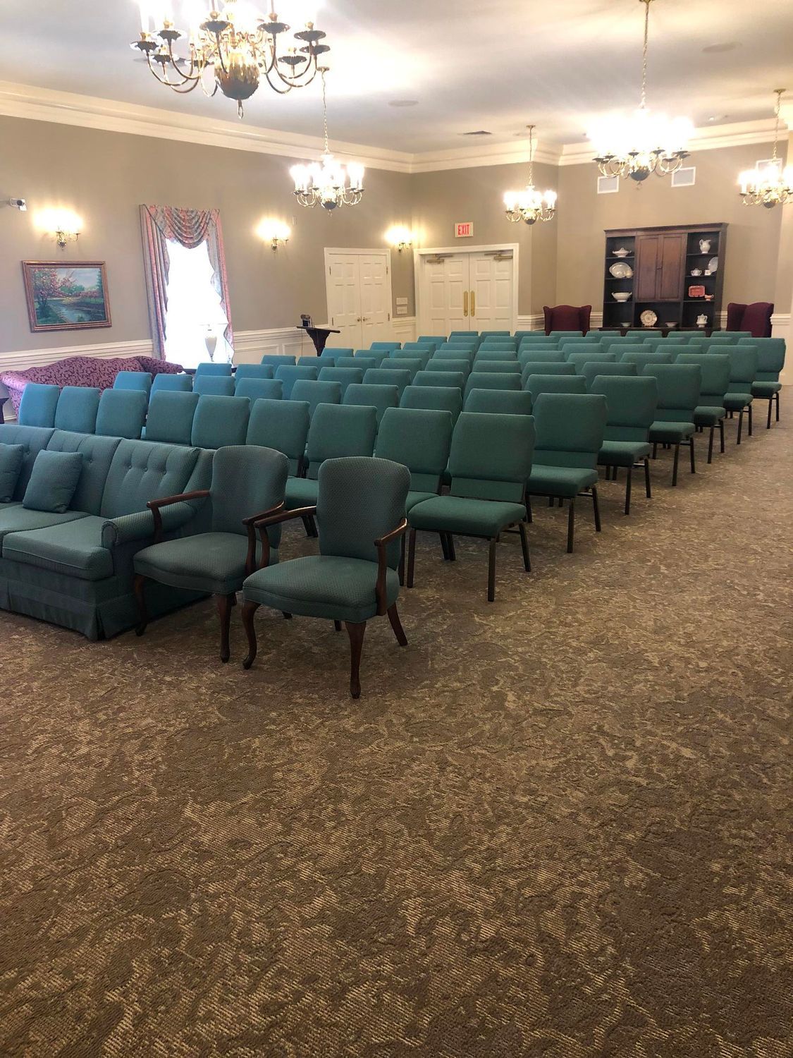 Empty church hall with rows of teal chairs and chandeliers on a carpeted floor