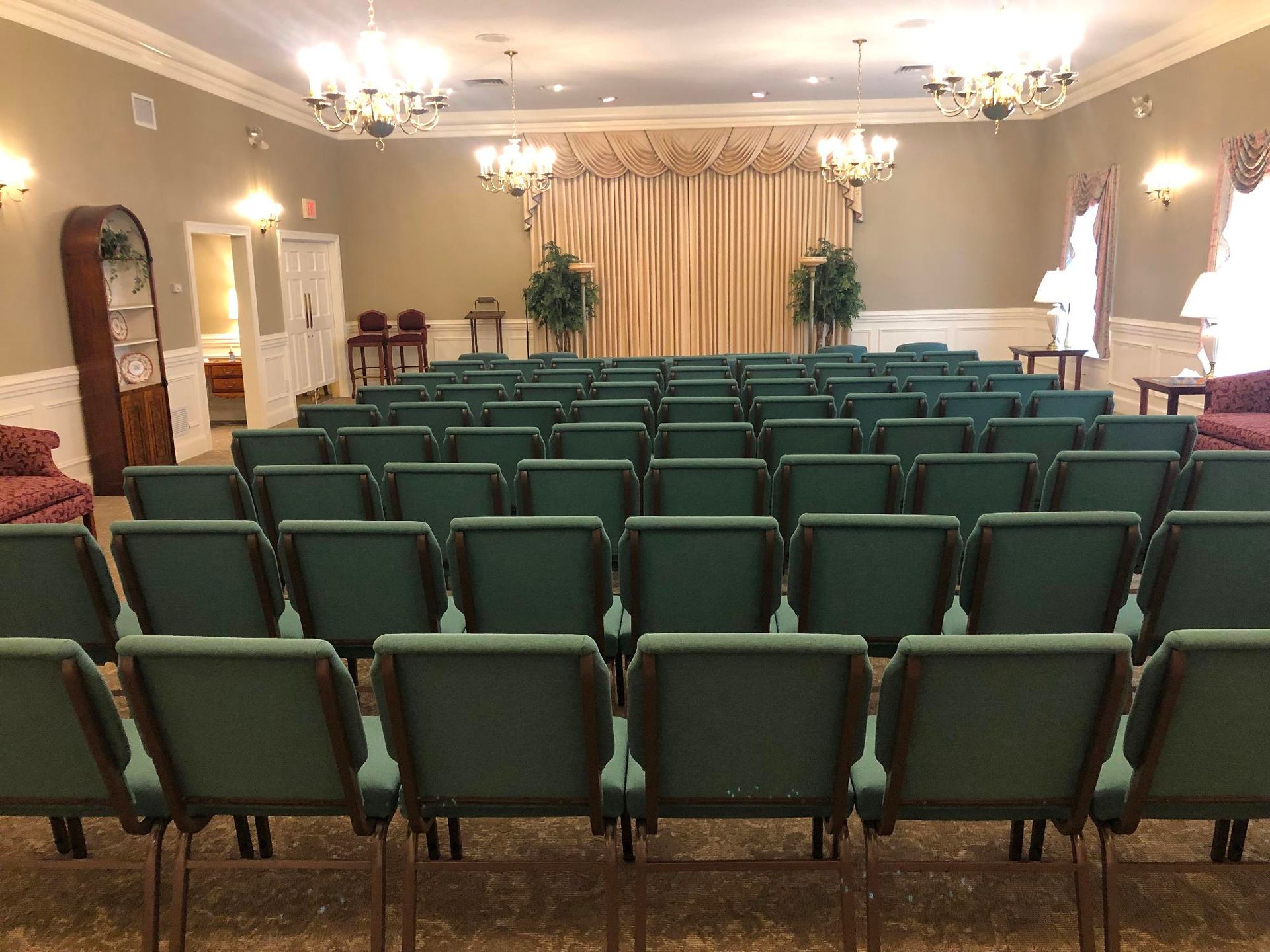 Empty banquet hall with rows of green chairs facing a curtained stage