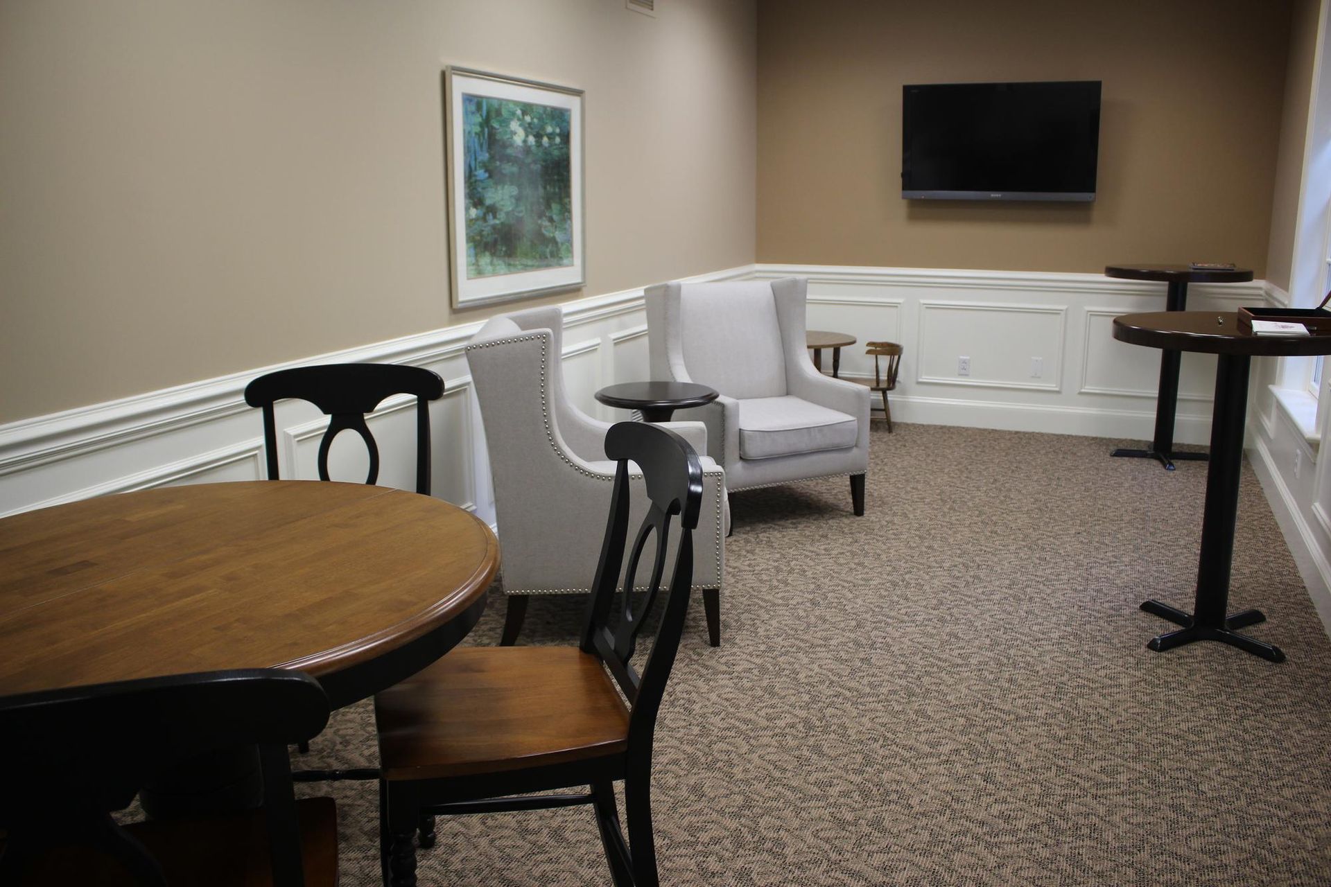Small lounge with round table, armchairs, wall art, TV, and carpeted floor.