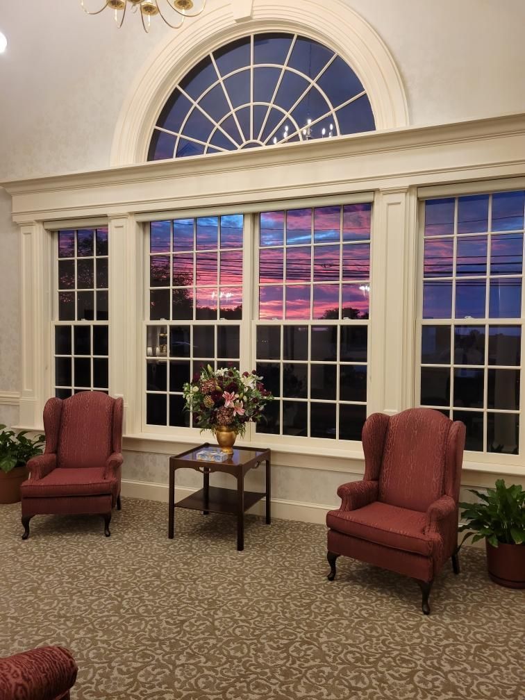Elegant room with two red armchairs, a small table, and a large arched window at sunset.