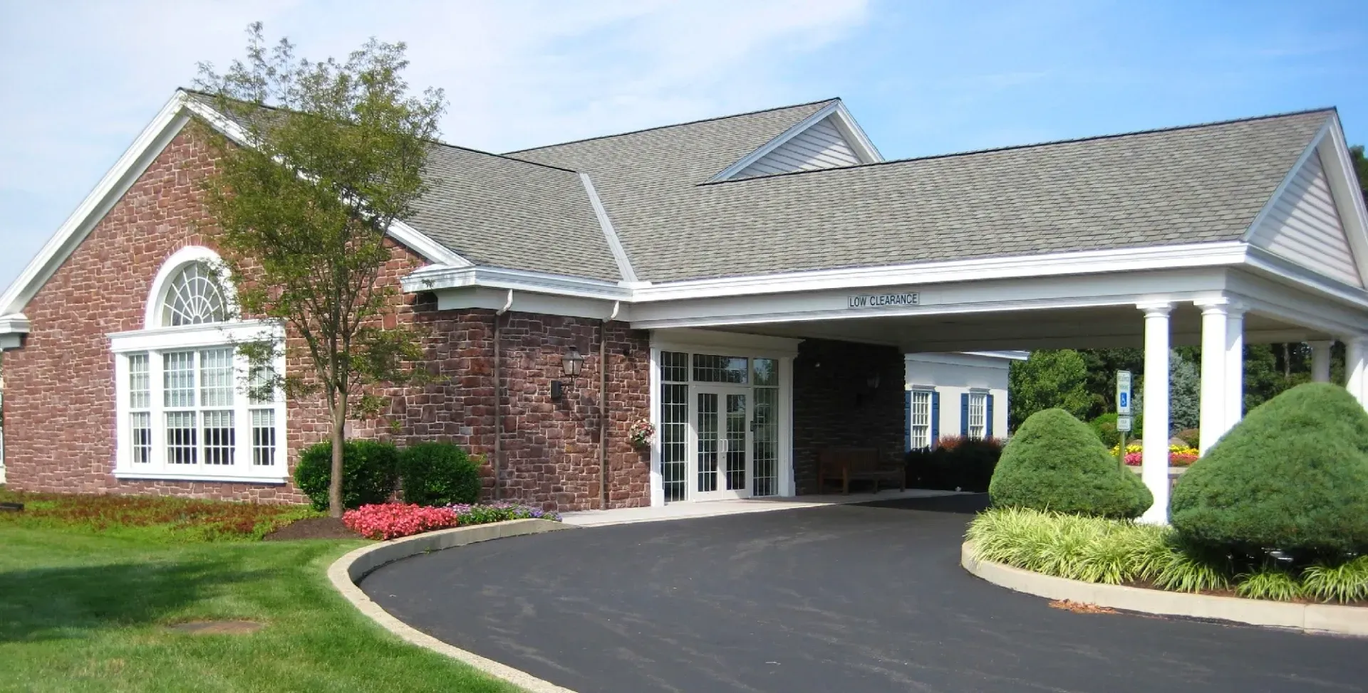 Brick house with white columns and arched window, viewed from a curved driveway and landscaped lawn