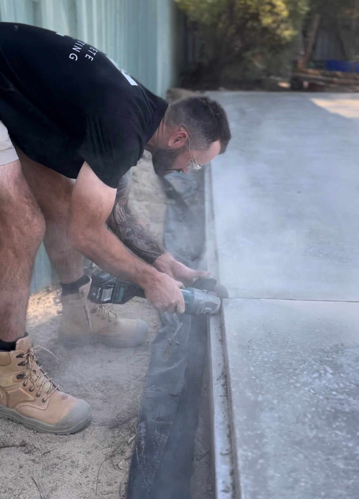 Worker using a concrete saw at the edge of a driveway, creating dust as he cuts the slab — Complete Concreting Riverina In Ashmont, NSW