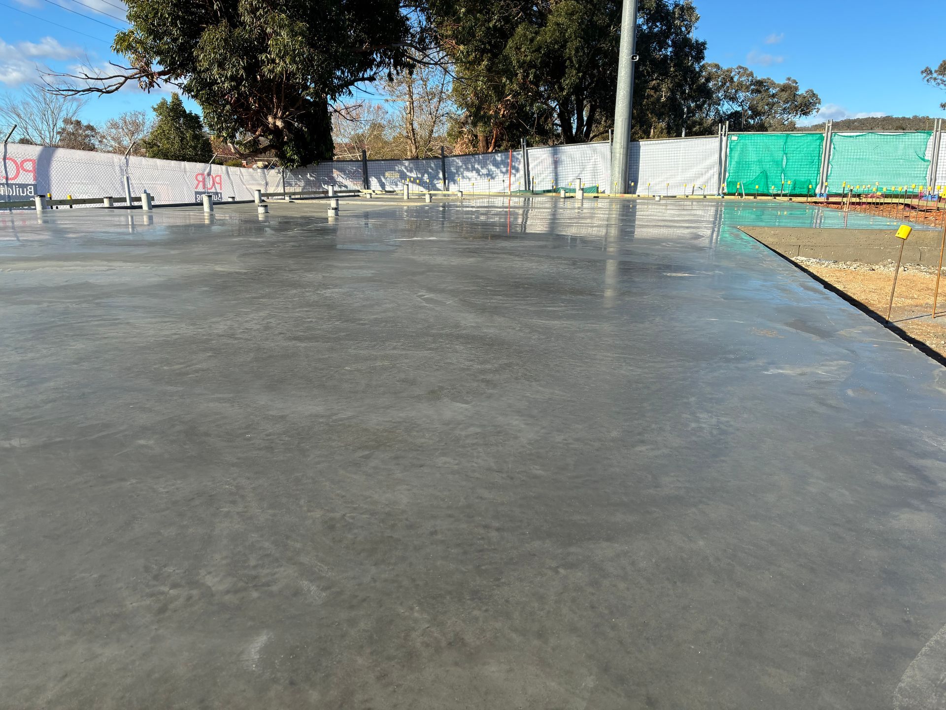 Freshly poured concrete slab beside a fence and trees under a clear sky — Complete Concreting Riverina In Ashmont, NSW