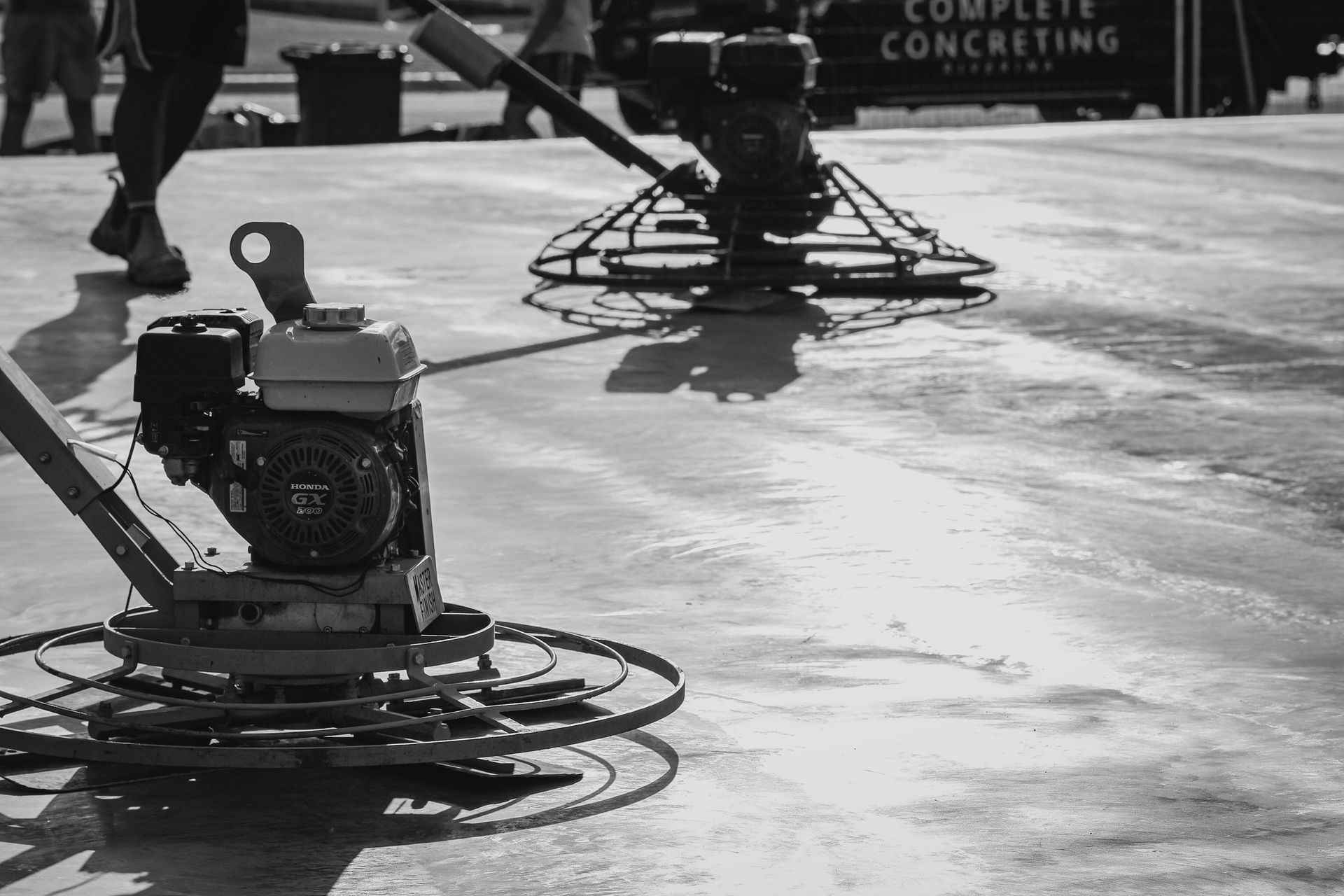 A worker uses a bull float to smooth freshly poured concrete on a sidewalk under construction — Complete Concreting Riverina In Ashmont, NSW