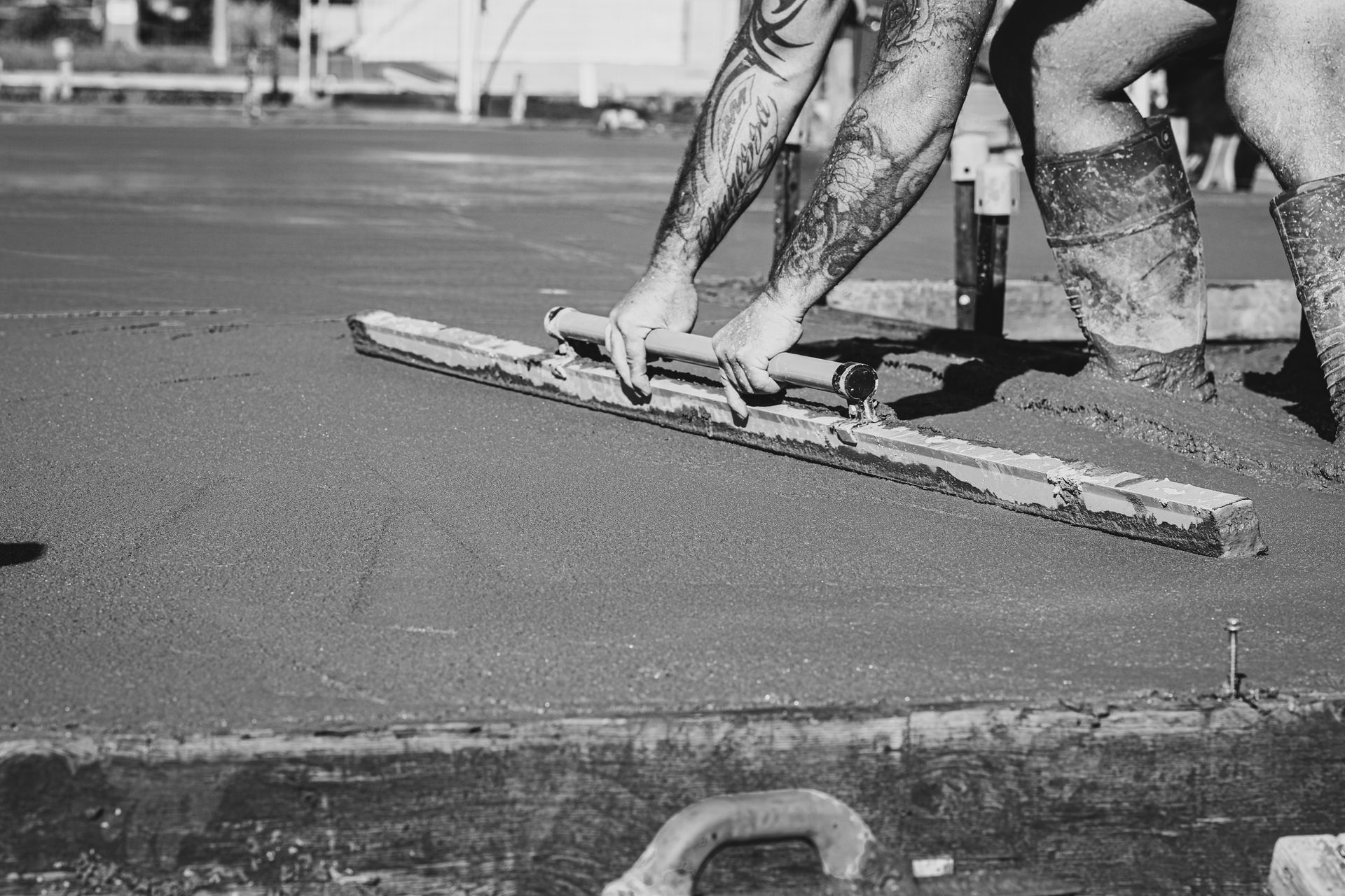 Workers smoothing wet concrete with a long screed on a street, black-and-white photo — Complete Concreting Riverina In Ashmont, NSW