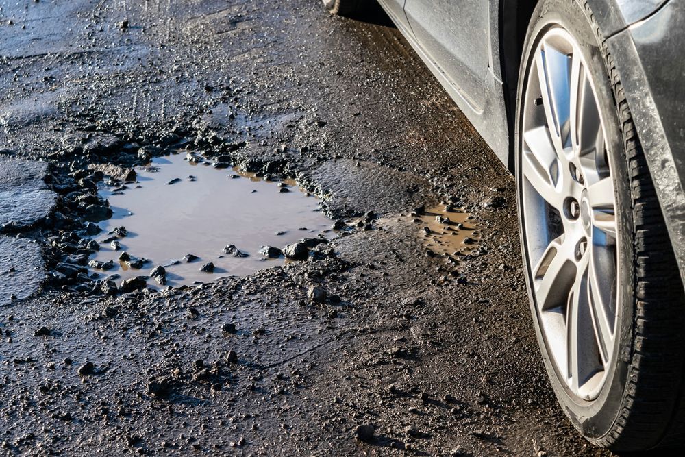 A car is parked on a muddy road next to a puddle.
